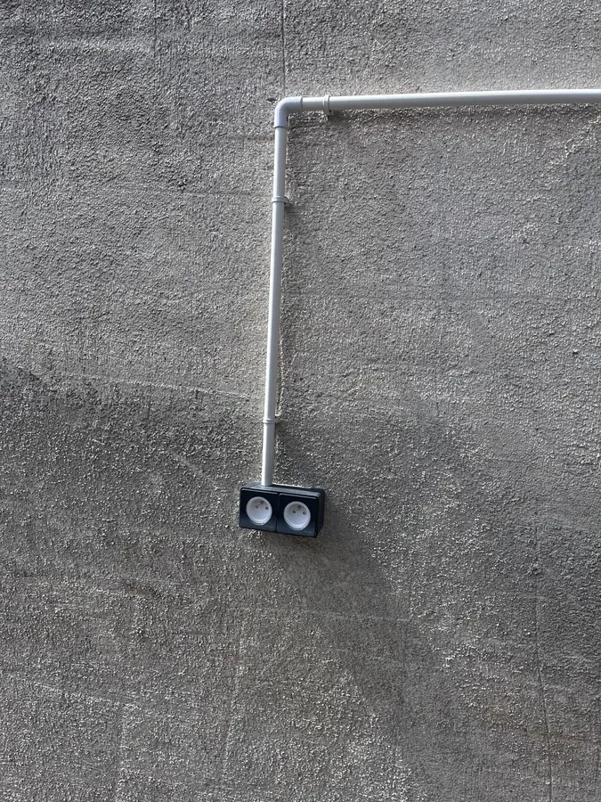 Prise double étanche alimentée par un conduit rigide fixé proprement le long d'un mur extérieur.