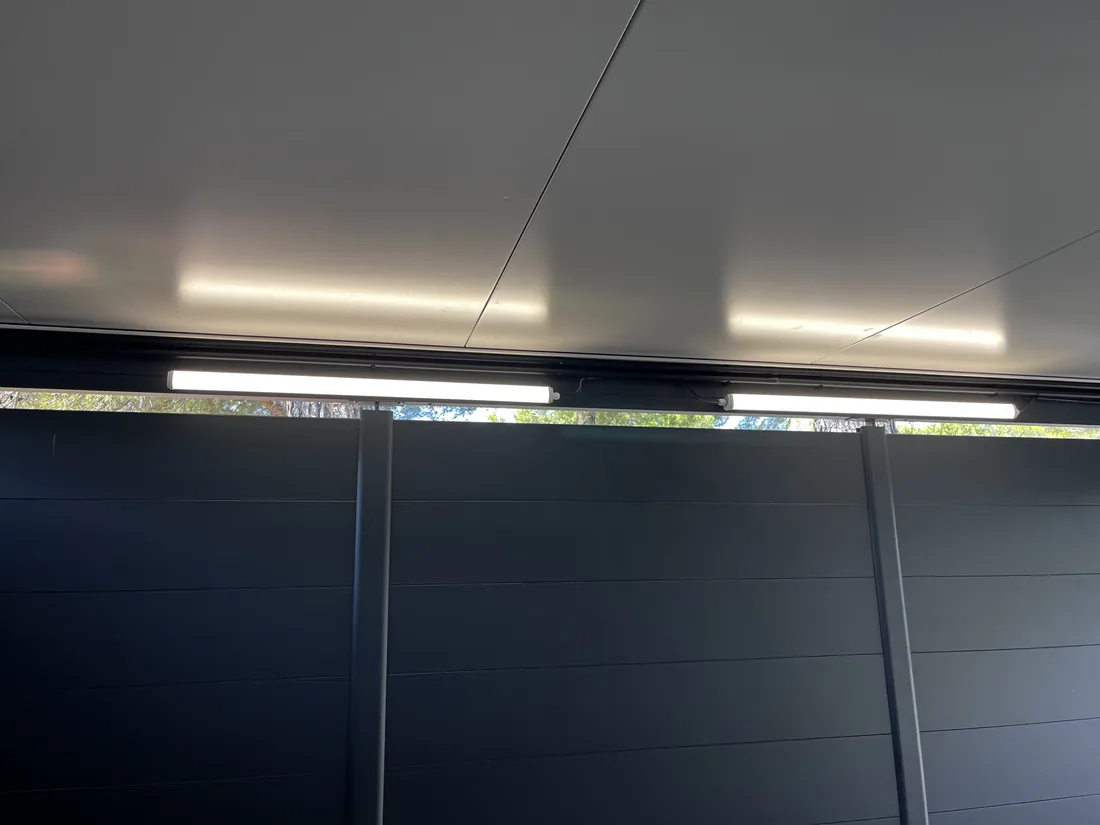 Deux réglettes LED alignées sous la toiture d'un carport, éclairant le plafond de manière homogène.